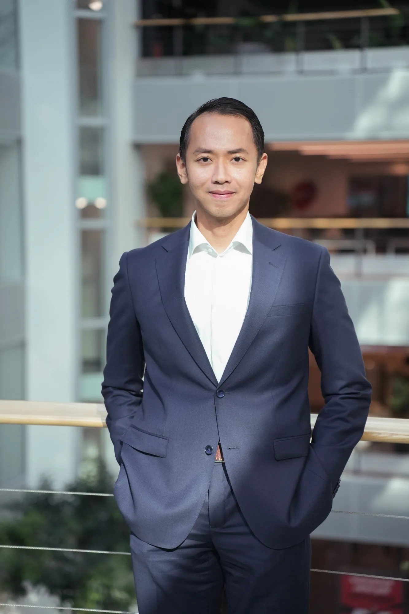 A professional portrait photo of Adrian Bex, standing by a railing in an office atrium.